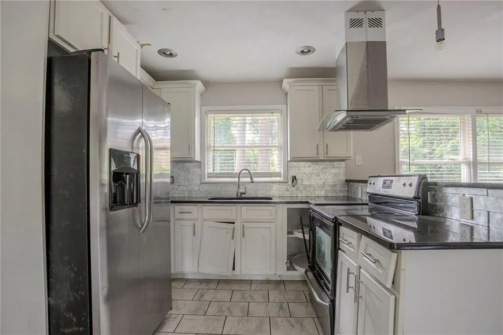 Kitchen featuring stainless steel appliances, island exhaust hood, dark countertops, decorative backsplash, and white cabinets