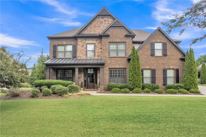 Craftsman-style house with a front lawn, brick siding, covered porch, and stone siding