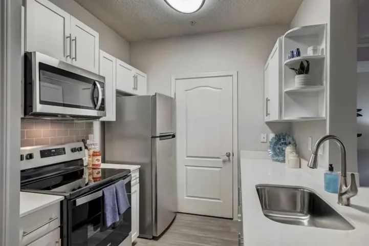 Kitchen with stainless steel appliances, sink, white cabinetry, a textured ceiling, and light hardwood / wood-style floors