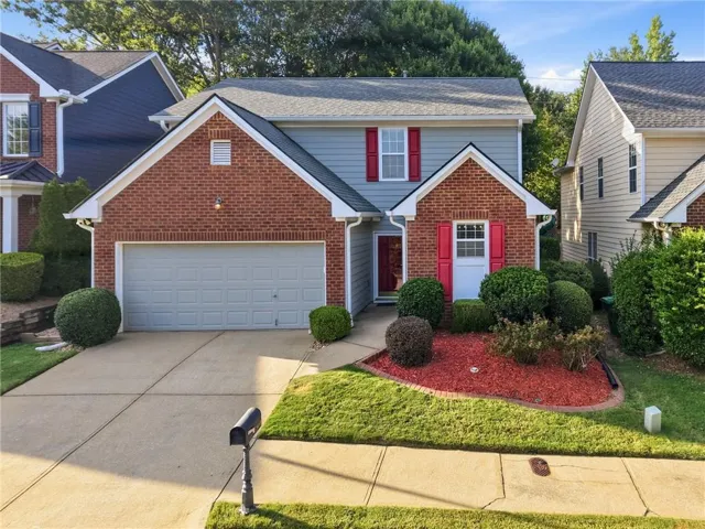 Brick and siding exterior featuring red shutters, a concrete driveway, an integrated garage, and landscaped front yard