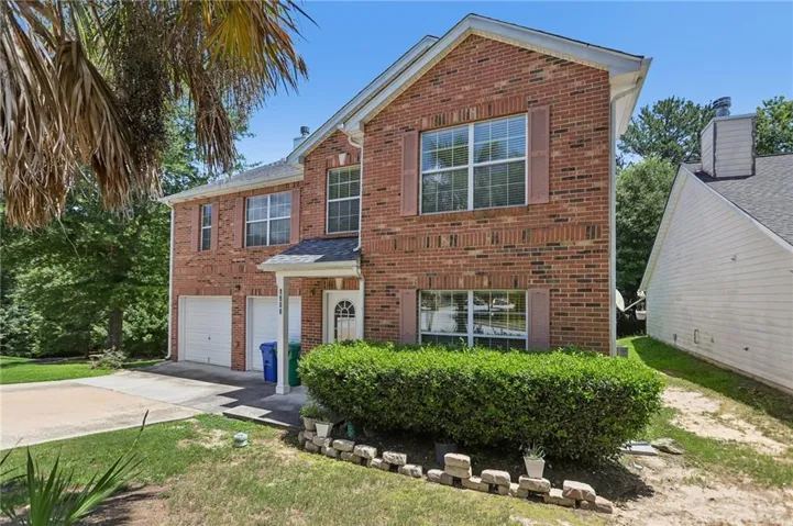 Brick-clad two-story residence featuring a two-car garage, white paneled garage doors, and a covered entry with an arched glass door