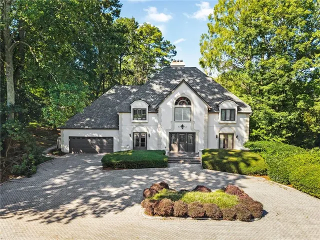 Stucco exterior with stone accents, a multi-car paver driveway, an integrated two-car garage, and mature perimeter landscaping