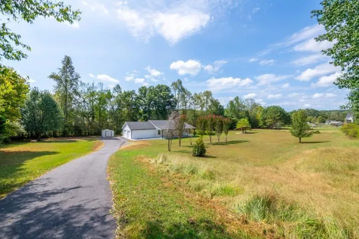 Expansive property featuring a paved driveway, detached storage shed, attached two-car garage, and mature trees throughout the landscape