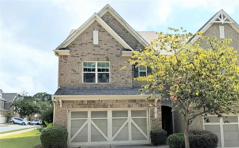 Brick exterior with multiple gables, two-car garage with decorative paneling, arched entry, and established landscaping