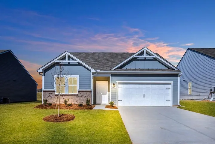 View of front facade with a garage, driveway, a lawn, brick siding, and roof with shingles