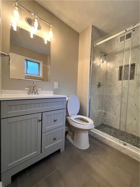 Bathroom featuring vanity, toilet, a shower with shower door, and a textured ceiling