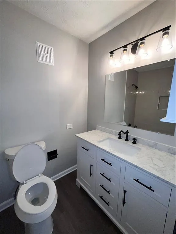 Bathroom featuring walk in shower, hardwood / wood-style floors, a textured ceiling, toilet, and vanity