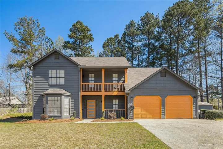 Two-story exterior with dark gray siding, prominent bay window, upper-level balcony, and double garage with orange doors