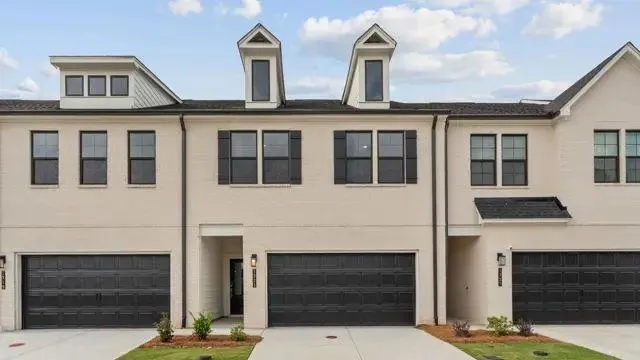 Painted brick exterior with black shutters, two dormer windows, attached garage, and concrete driveway