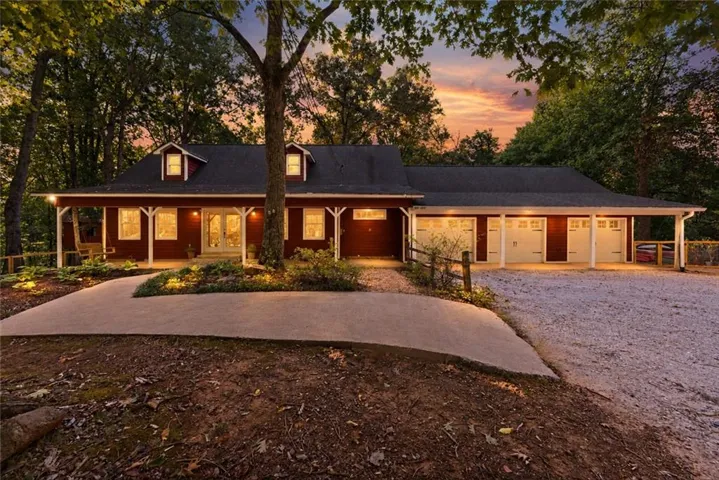 Red exterior siding with white trim, dormer windows, covered front porch, integrated three-car garage, and gravel driveway
