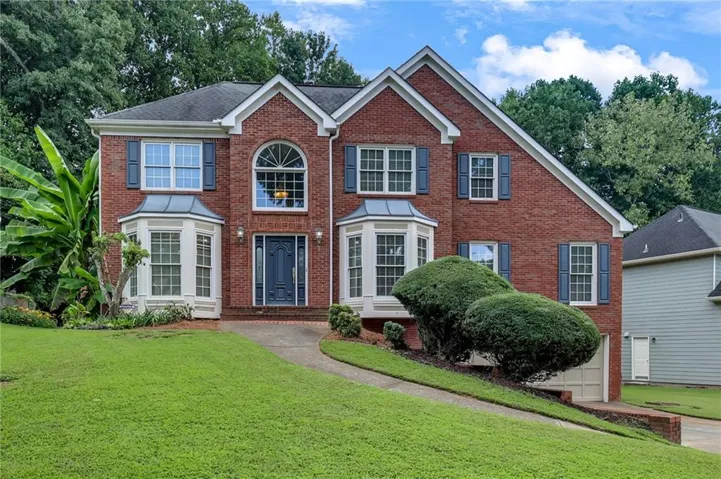 Brick facade residence featuring a prominent arched window, multiple bay windows, and a two-car garage
