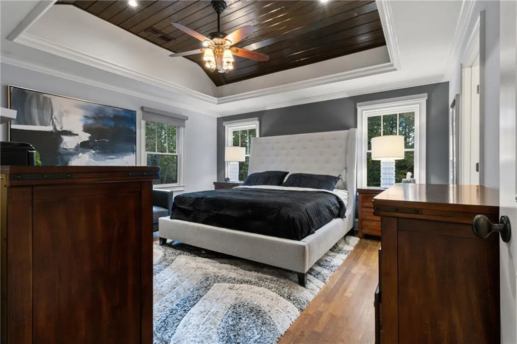 Bedroom featuring a raised ceiling, wooden ceiling, wood finished floors, crown molding, and multiple windows