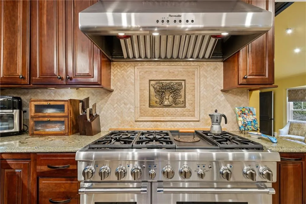Kitchen featuring ventilation hood, decorative backsplash, double oven range, and light stone countertops
