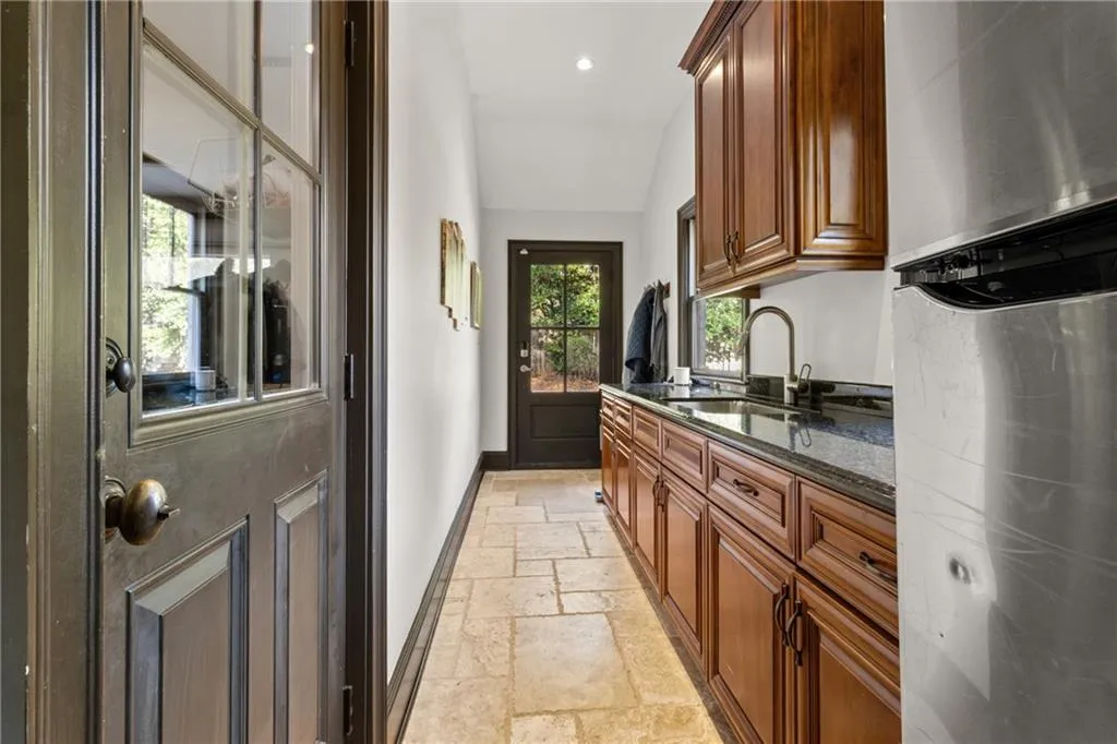 Kitchen featuring dark stone countertops, freestanding refrigerator, stone tile flooring, brown cabinetry, and recessed lighting