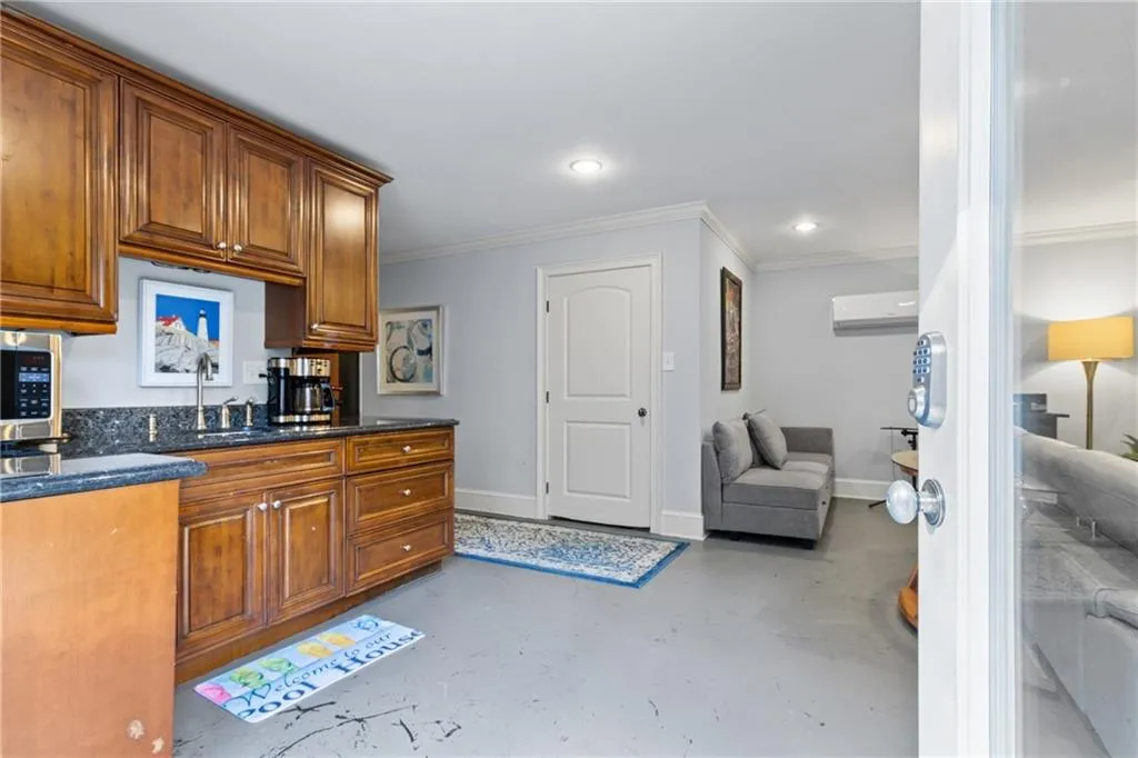 Kitchen featuring finished concrete flooring, dark stone countertops, brown cabinetry, crown molding, and a wall mounted AC