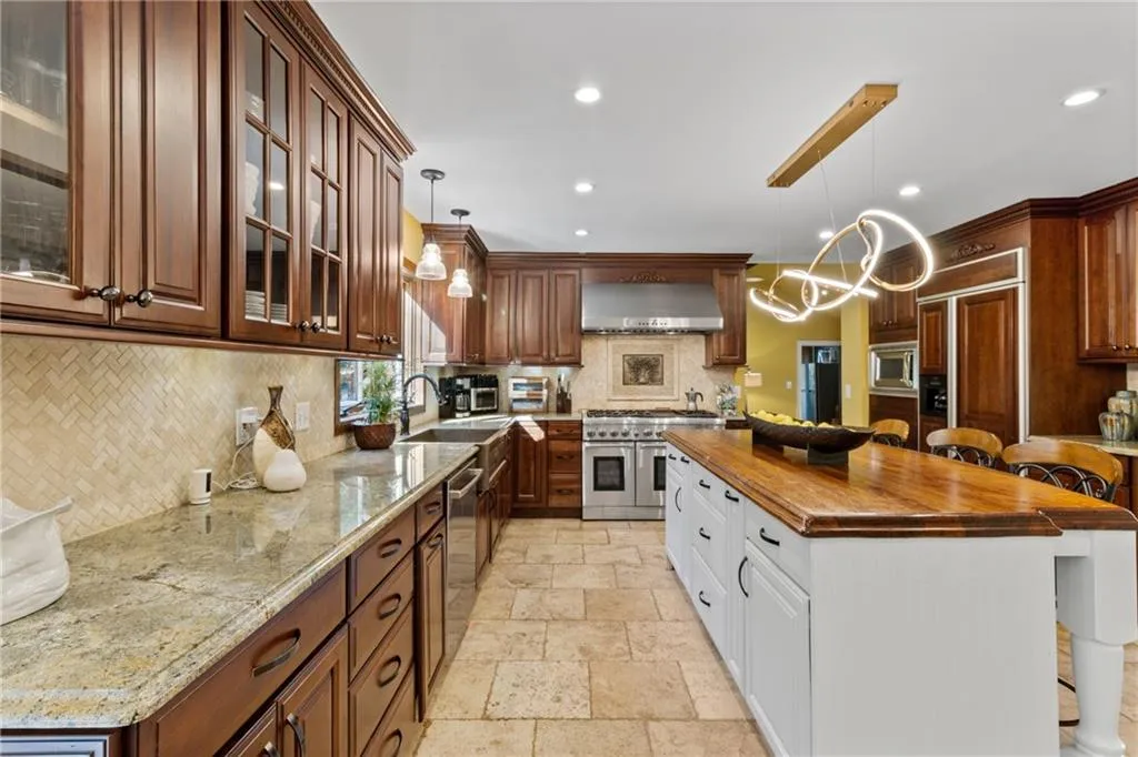 Kitchen with a kitchen breakfast bar, decorative light fixtures, tasteful backsplash, white cabinets, and built in appliances