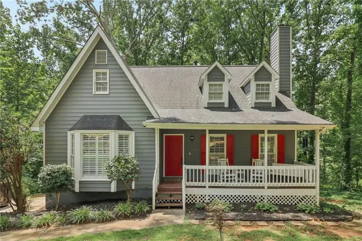 Gable roofline, bay window with louvered shutters, covered porch with white railing, and a prominent chimney