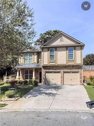 Multi-story residence featuring a two-car garage, stone and stucco exterior, prominent gables, and a concrete driveway
