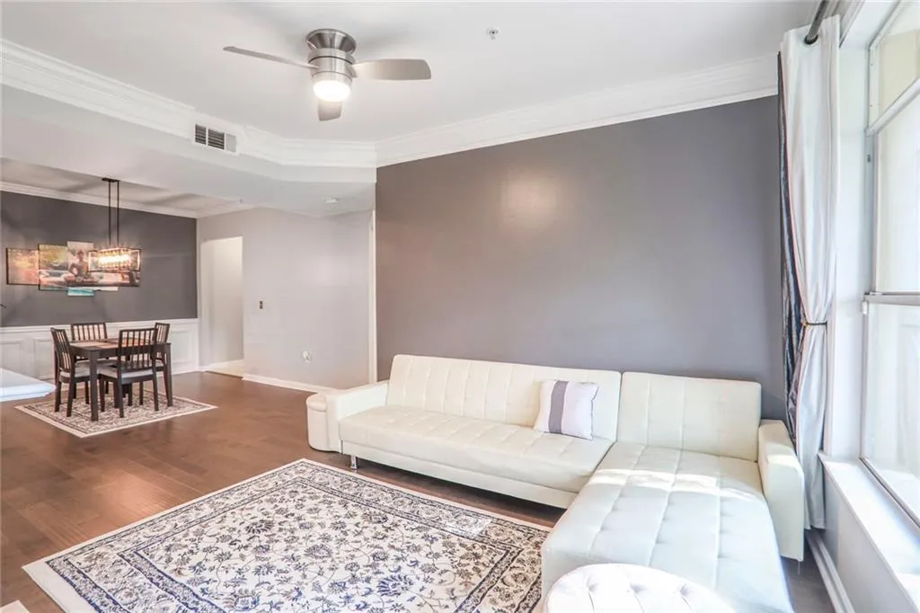 Living room with a chandelier, wood finished floors, ornamental molding, a ceiling fan, and baseboards