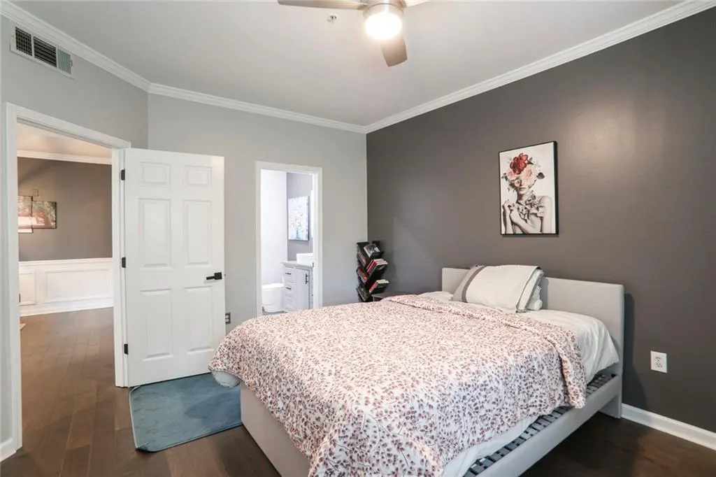 Bedroom with crown molding, dark wood-style flooring, connected bathroom, a ceiling fan, and baseboards