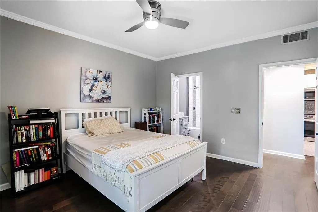 Bedroom with crown molding, dark wood-style flooring, baseboards, ensuite bath, and a ceiling fan
