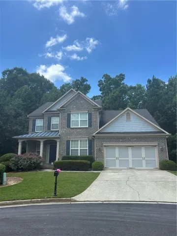 Brick exterior with dark shutters, covered front porch, a two-car garage, and established landscaping