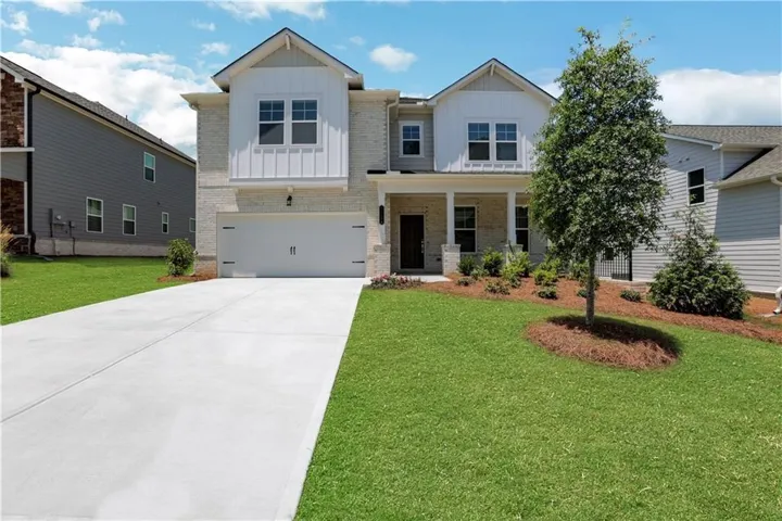 Two-story exterior with light brick and white vertical siding accents, featuring a front-facing attached garage and a covered porch with white columns
