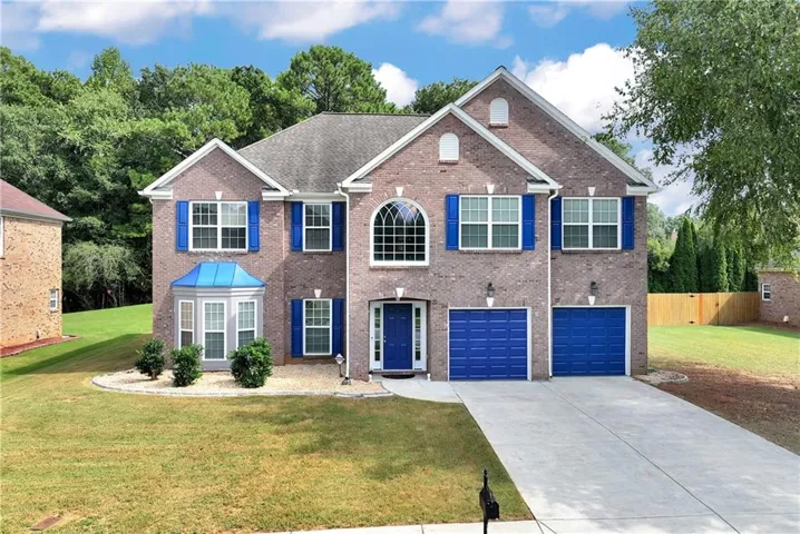 Brick facade with blue shutters, a bay window with a blue metal roof, and a two-car garage