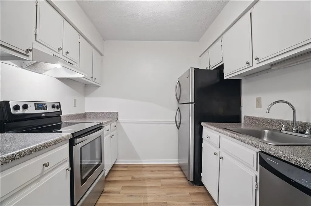 Kitchen featuring appliances with stainless steel finishes, a sink, white cabinetry, light wood-style floors, and a textured ceiling