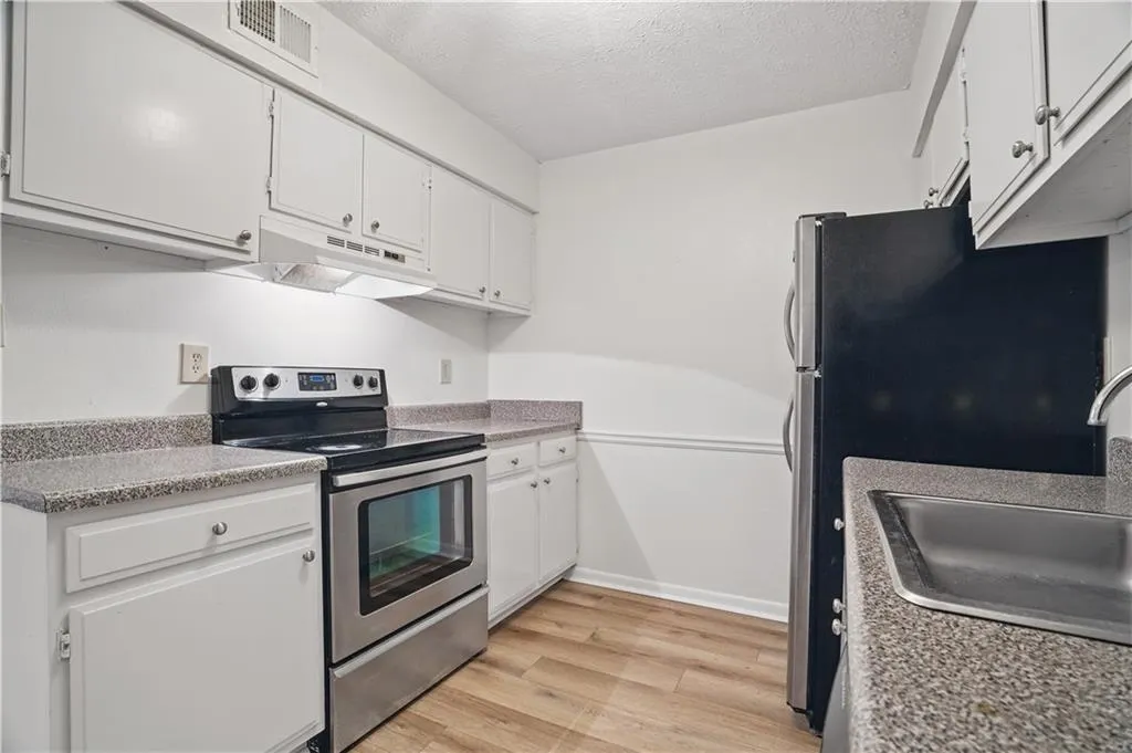 Kitchen featuring stainless steel electric range, under cabinet range hood, a sink, light wood-style flooring, and white cabinets