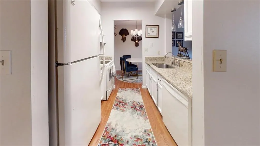 Kitchen with light wood-style floors, white appliances, white cabinets, light stone counters, and a chandelier