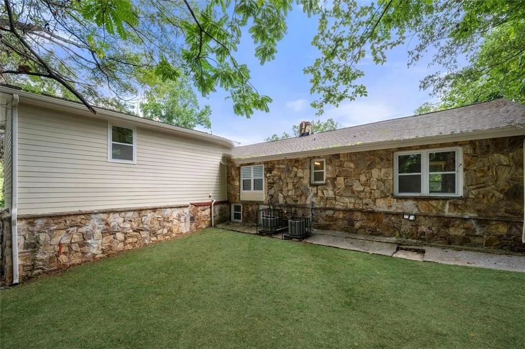 Rear view of property featuring a yard, stone siding, a chimney, and a patio