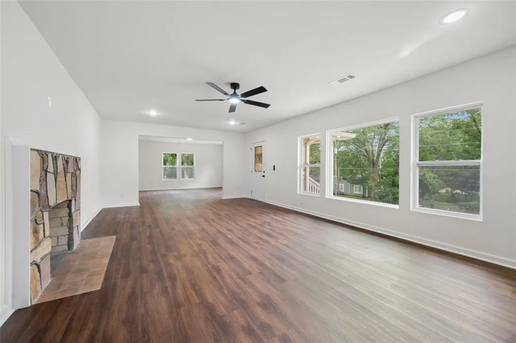 Unfurnished living room with dark wood-style flooring, ceiling fan, a stone fireplace, and recessed lighting