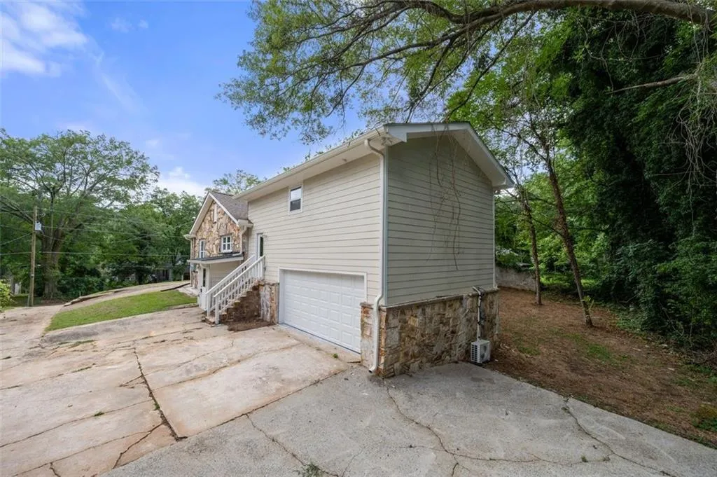 View of side of property featuring stone siding, driveway, an attached garage, and stairway