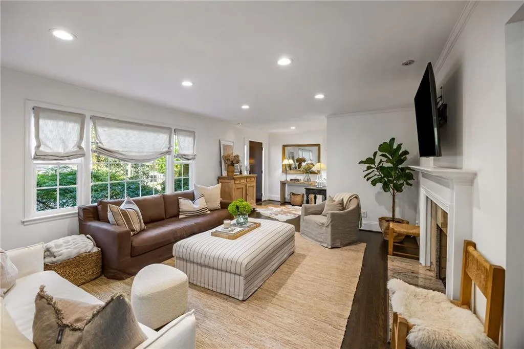 Recessed lighting illuminates the living space featuring large windows, dark wood-finish flooring, and a built-in fireplace with a white mantel