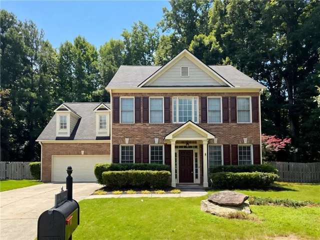 Brick facade home featuring a two-car garage, mature landscaping, and a covered entryway
