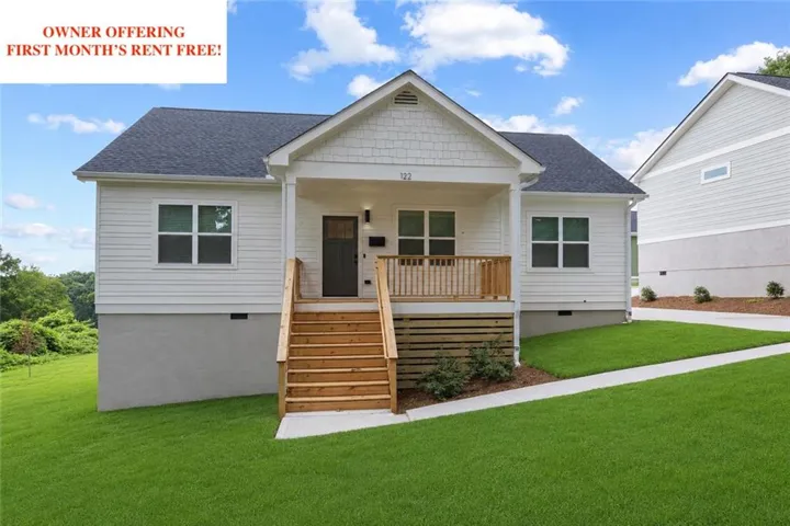 White siding exterior with a dark shingle roof and a covered front porch featuring natural wood stairs and railing