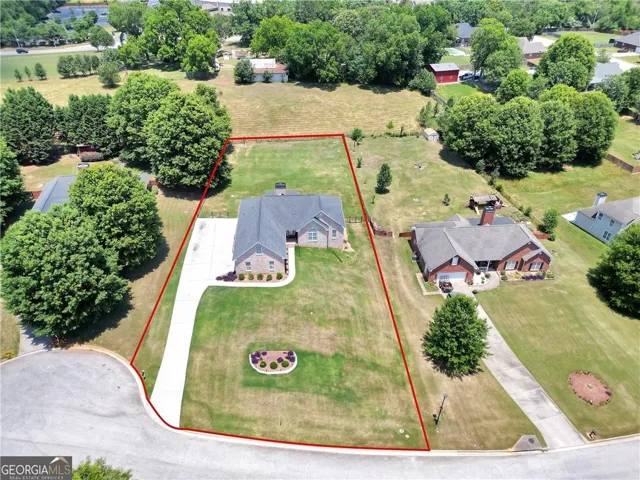 Brick facade with a dark shingle roof, expansive green lawn, and a paved driveway leading to the street