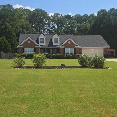 Brick exterior with a dark shingle roof, two dormer windows, and a two-car garage with arched paneling