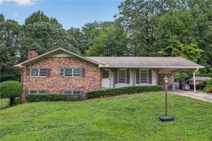 Brick and siding exterior with a covered carport, mature trees, and landscaping