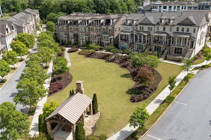 Expansive green space with manicured lawn and mature trees, bordered by multi-story townhomes