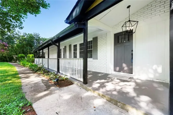 Covered front porch featuring a dark gray front door with transom window, white brick and board and batten siding, black gutters, and a geometric hanging light fixture
