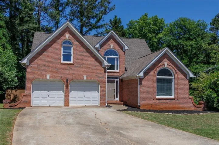 Brick exterior featuring a two-car garage, arched windows, and a gabled roofline