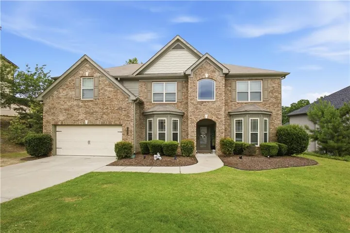 Two-story brick facade residence featuring a prominent arched entryway, bay windows, and an integrated two-car garage