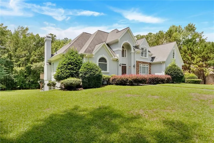 View of front of home with a front lawn, stucco siding, a chimney, and a shingled roof