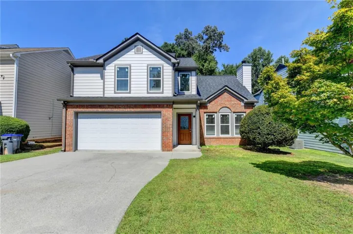Brick and siding exterior with a two-car garage, mature landscaping, and a paved driveway