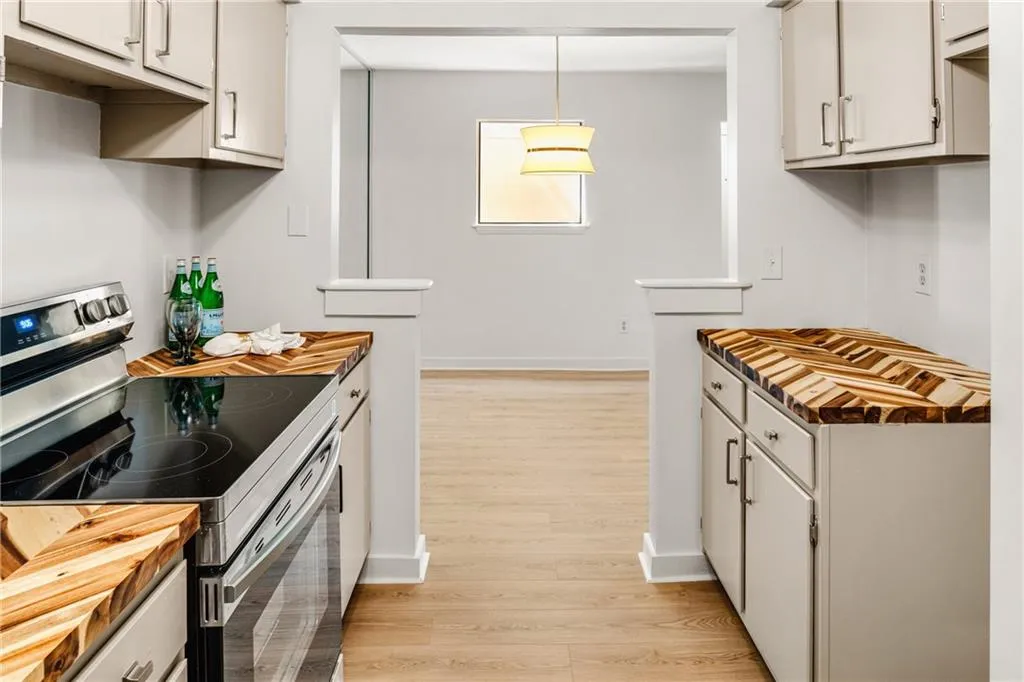 Kitchen with stainless steel range with electric cooktop, light wood-style floors, wood counters, decorative light fixtures, and white cabinets