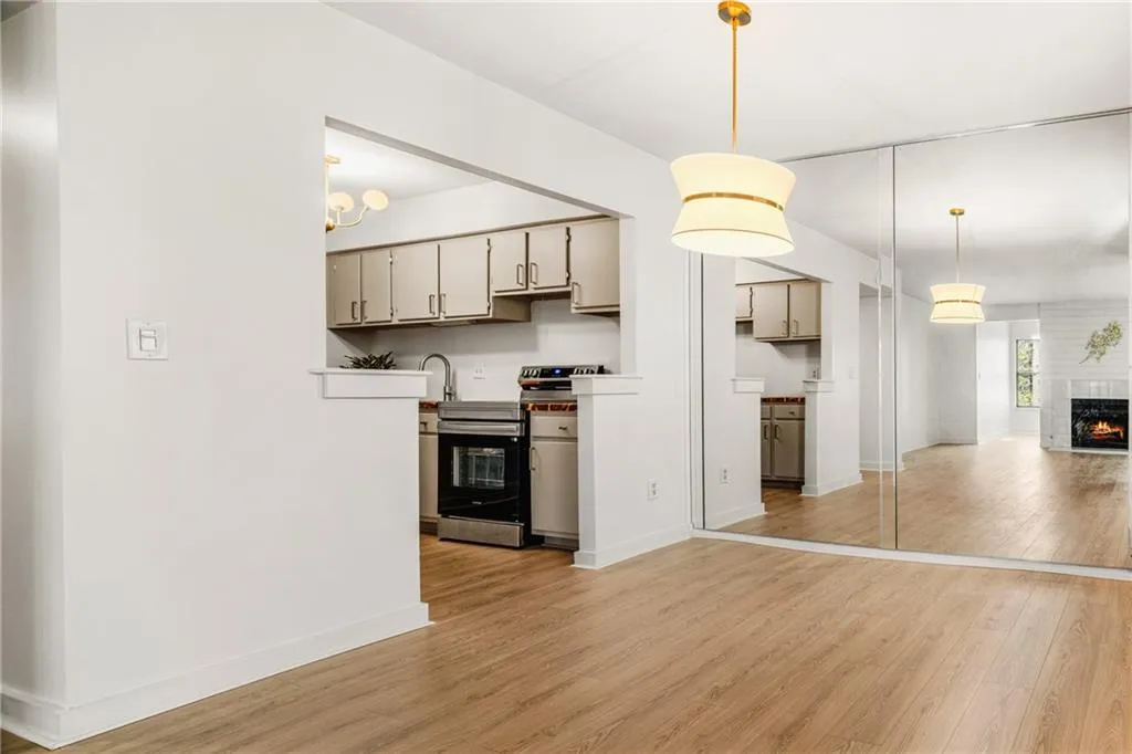Kitchen with light wood finished floors, a fireplace, stainless steel electric range, hanging light fixtures, and open floor plan
