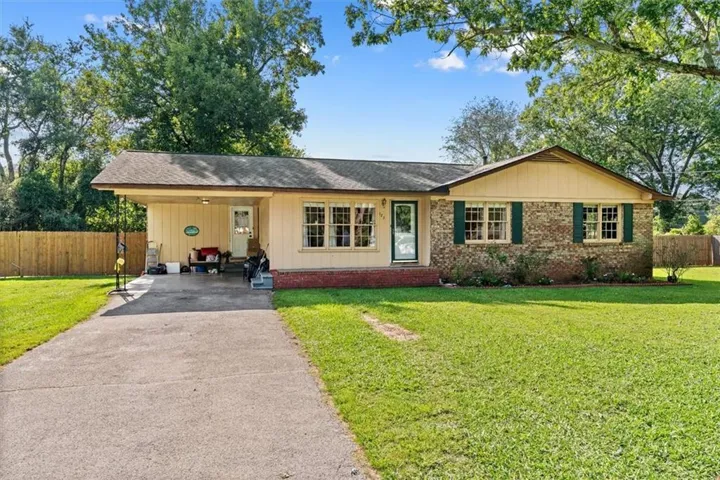 Brick and siding exterior with a covered carport, mature trees, a fenced backyard, and a paved driveway