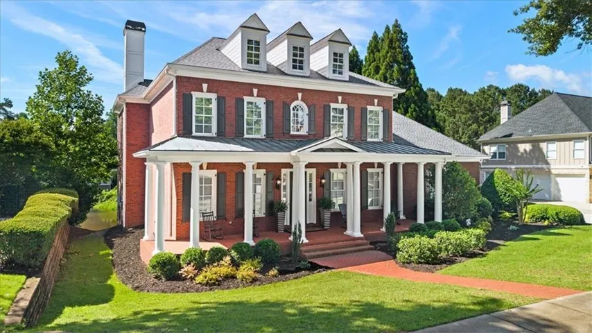 Traditional brick residence featuring a full-width covered porch with white columns, dormer windows, and a chimney